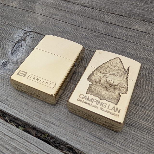 Two brass Zippo-style lighters laser engraved with custom camping event branding